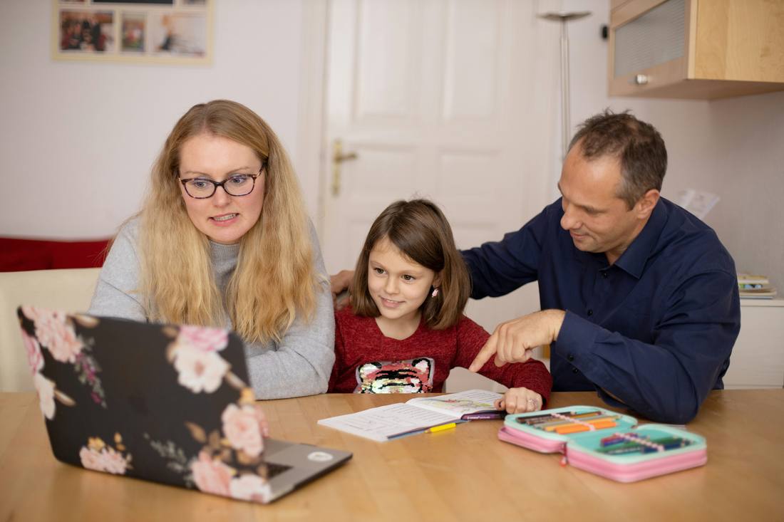 Parents helping their daughter study at the kitchen table